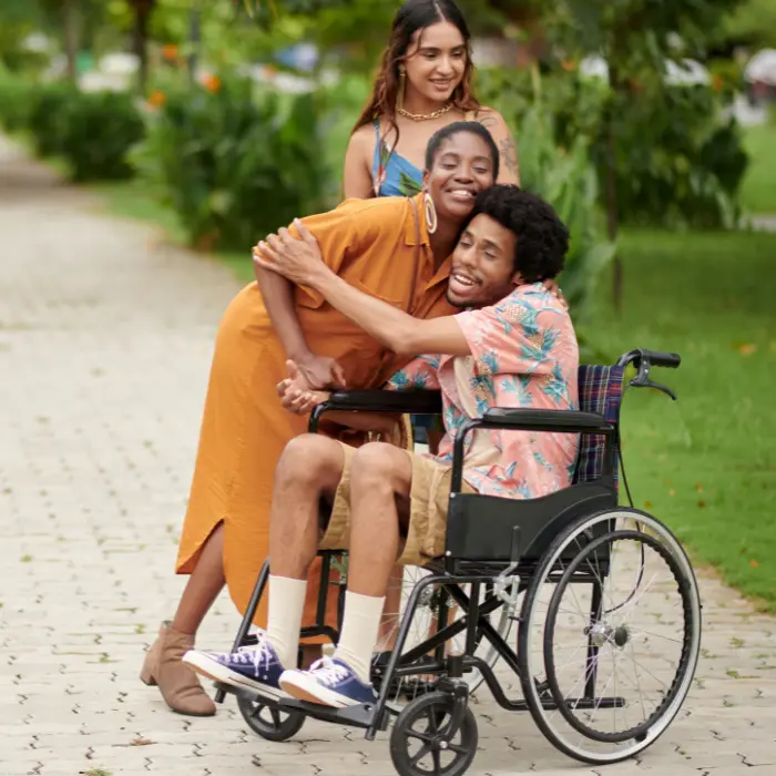 Disabled man in wheelchair outside with friends hugging one of them