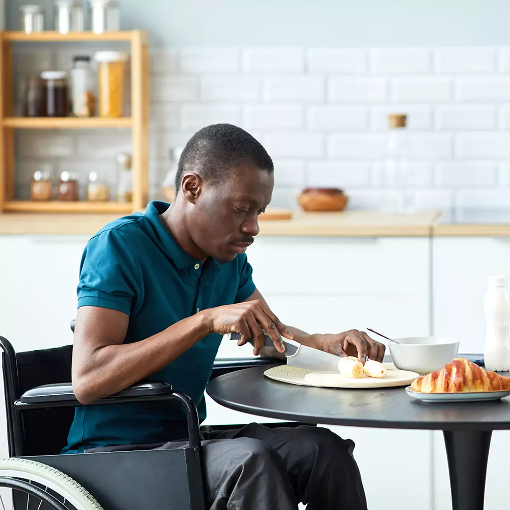 A disabled man in a wheelchair cutting up a banana