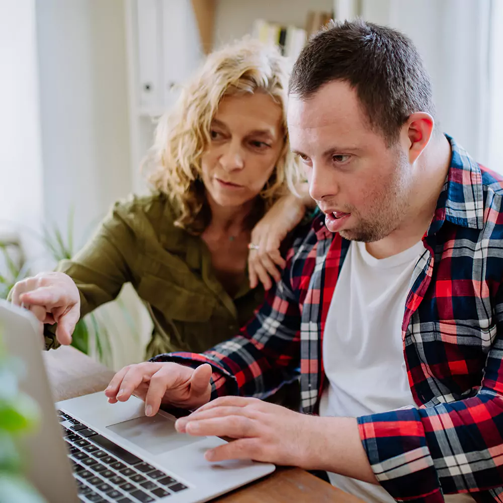 a down syndrome man using a computer with his care giver
