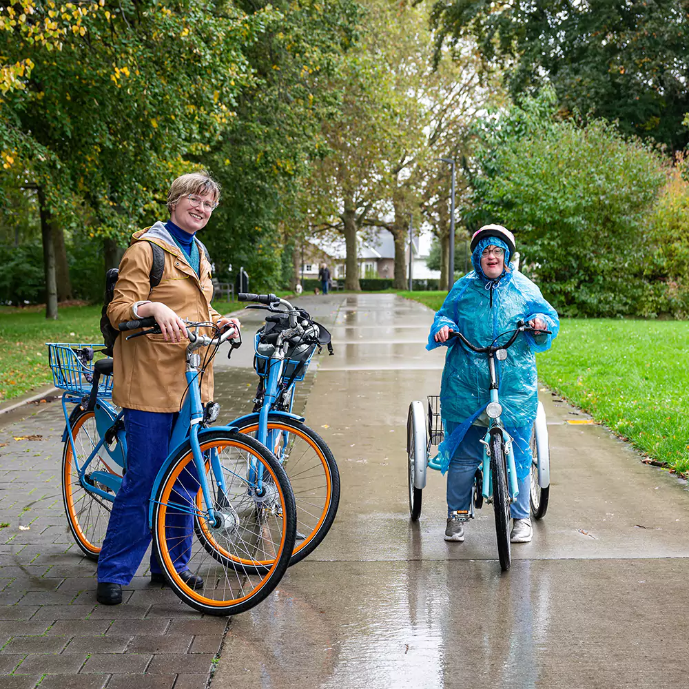 A down syndrome woman riding her bike outdoors with her carer